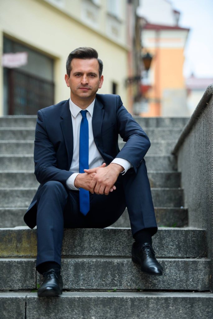 Robert Wardzała w garniturze, siedzący na schodach