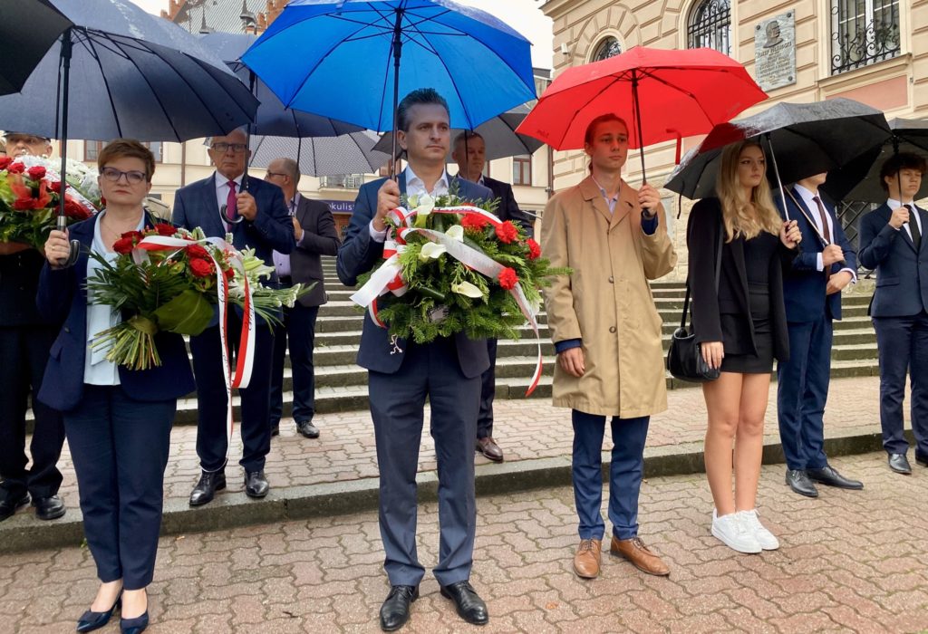 Uczestnicy uroczystości pod parasolami z kwiatami w dłoniach