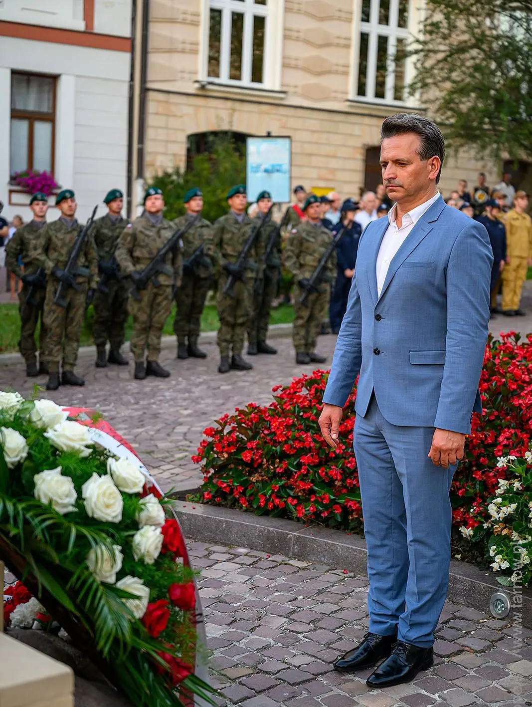 Robert Wardzała — przy wiązankach kwiatów, z żołnierzami w tle