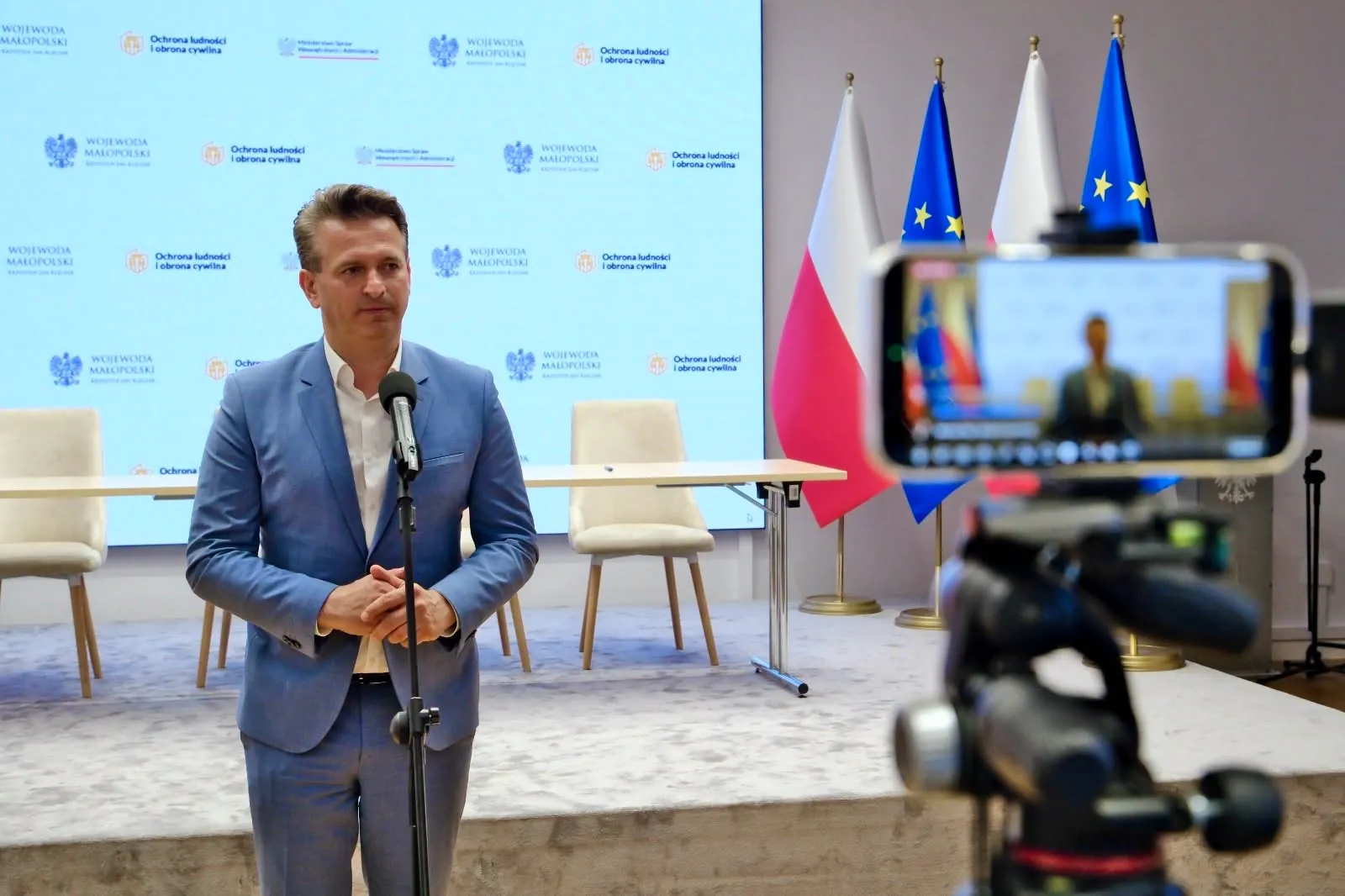 Robert Wardzała — przed kamerą na tle planszy o ochronie ludności